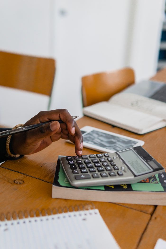 A person using a calculator on a wooden table, surrounded by books and stationery.